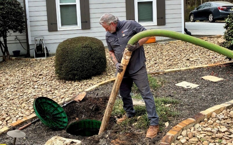 A licensed Guardian technician feeding the pump hose into an open septic tank lid at a home